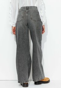 Jean taille haute gris à jambes larges, en denim, avec une finition délavée, cinq poches et des coutures contrastantes visibles le long des coutures.