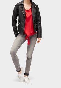 Sort læder bikerjakke, rød ærmeløs top med sløjfe, lysegrå stramme jeans, hvide sneakers med sløjfe-detalje.