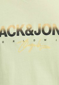 Hellgrünes Baumwoll-T-Shirt mit auffälligem schwarzen und goldfarbenen Farbverlauf-Text "BLACK&JON" sowie charakteristischem Design, glatter Textur und Rundhalsausschnitt.