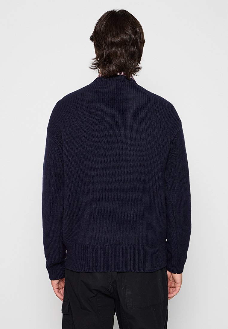 Marineblauer Strickpullover mit hohem Kragen, gerippter Textur und abgesenkten Schultern. Verfügt über einen geraden Saum und strukturierte Details an den Ärmeln.