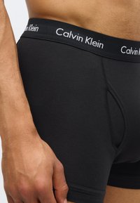 Boxerii scurți din bumbac negri au o croială strânsă, o bandă elastică cu logo-ul Calvin Klein și o textură netedă, cu o deschidere funcțională la zips.