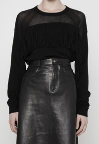Pull noir en tricot avec détails en maille et accents de franges, associé à une jupe en cuir noire taille haute avec une texture lisse et une couture frontale.