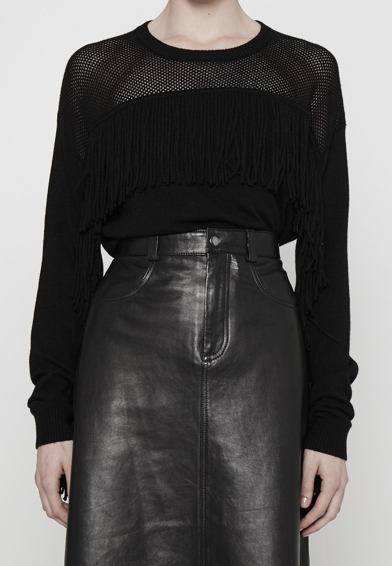 Pull noir en tricot avec détails en maille et accents de franges, associé à une jupe en cuir noire taille haute avec une texture lisse et une couture frontale.