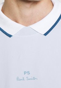 Polo tričko v světle šedé látce s bílým límcem a modrým pruhovaným lemem. Vyšité "PS" a "Paul Smith" v světle modré.