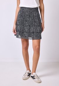 Jupe à volants noir et blanc avec un motif floral, fabriquée en tissu léger, taille élastique, associée à des baskets décontractées.
