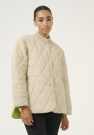 Giacca trapuntata beige con motivo a rombi, colletto a coste e bottoni a pressione. Foderata con tessuto verde a contrasto sui polsini.