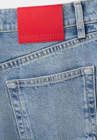 Jean en denim bleu clair avec une poche arrière et une étiquette en cuir rouge cousue embossée de "MNG DENIM" près de la taille.