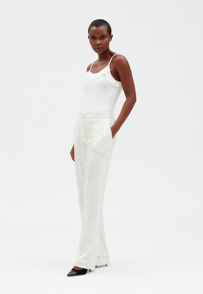 Top bianco con spalline arricciate, abbinato a pantaloni argentati brillanti e con paillettes. Design slim fit, gamba dritta, con scarpe nere a punta.