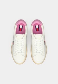 Vita skinnsnickers med beige sula, rosa foder och Tommy Jeans-logotyp på tungan och sidan, visad från ovan.