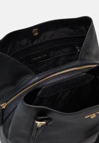 Sort læderhåndtaske med en struktureret overflade, guldfarvet hardware, indvendige lynlåslommer og en stofforing med et gentagende logo mønster.