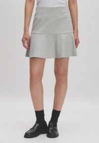 Grauer Baumwollrock mit einem ausgestellten Saum, ausgestattet mit einem figurbetonten Bund und geschichtetem Design. Trägt schwarze Schuhe und Socken.