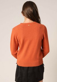 Pull en maille orange avec un ourlet côtelé, présentant un col rond et un petit détail décoratif à l'arrière. Texture douce, manches longues.