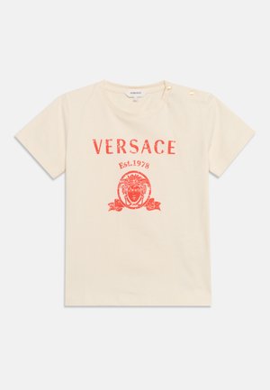 T-shirt crème à manches courtes avec logo Versace rouge, motif tête de Méduse, texte "Est. 1978" et deux boutons dorés sur l'épaule.