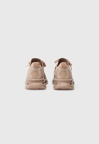 Scarpe sportive beige con una parte superiore testurizzata, linguetta posteriore e colletto imbottito. La suola presenta un design arrotondato per il comfort.