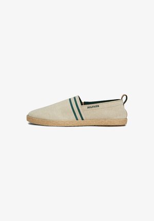 Espadrille beige à enfiler avec deux bandes latérales vert foncé, texte "HILFIGER", semelle tissée et languette à l'arrière.