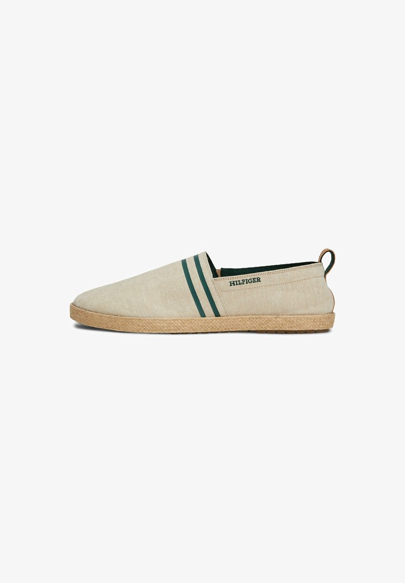 Espadrille beige à enfiler avec deux bandes latérales vert foncé, texte "HILFIGER", semelle tissée et languette à l'arrière.
