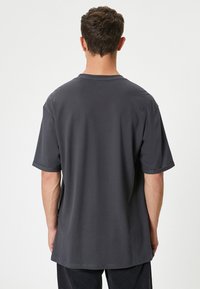 Grå bomulds t-shirt med korte ærmer, rund hals og en afslappet pasform. Har en glat tekstur og en lige kant forneden.