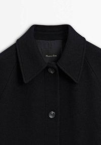 Sort uldfrakke med spids krave, enkelt knaplukning og struktureret stof. Indvendig label viser "Massimo Dutti."