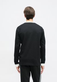 Melnā garroku krekls ar apaļu kakla izgriezumu, kam kontrastējoši balti aproces un gluda tekstūra. Vienkārša, sportiska piegriezuma.