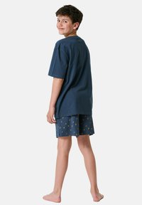 Navy blue cotton T-shirt with short sleeves paired with navy shorts featuring a sun pattern in orange. Child standing barefoot, facing back.