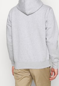Sudadera gris de material suave y cepillado con una gran capucha, puños y cintura acanalados, que presenta un corte clásico y un diseño minimalista.