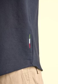 Polo shirt navy con maniche corte, caratterizzato da un tessuto testurizzato e un ricamo del tricolore italiano in verticale sulla cucitura laterale.