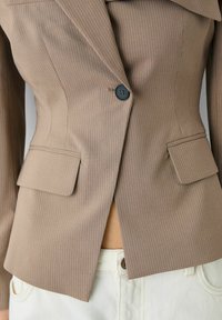 Blazer marron à rayures fines avec une coupe ajustée, dotée d'un col cranté, d'une fermeture à un bouton et de deux poches à rabat à l'avant.