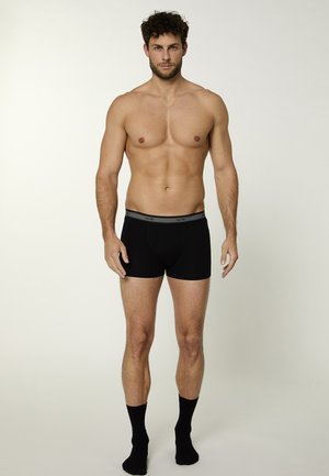 Boxer neri con fascia grigia in vita, caratterizzati da una texture morbida e liscia, indossati da un modello maschile in piedi con calzini.