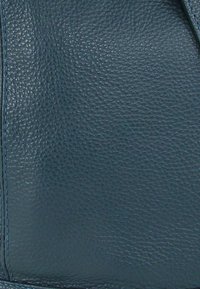 Diepblauw gestructureerd leer met een korrelige structuur en zichtbare stiksels. Het materiaal is soepel met een lichte glans, wat het vakmanschap benadrukt.