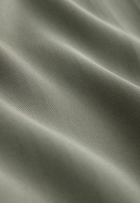 Olíva zöld színű textil sima textúrával, finom bordázott mintázattal. Az anyag könnyűnek és rugalmasnak tűnik, enyhe fényességgel.