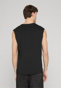 Black sleeveless shirt made of soft fabric, featuring a rounded hem and a relaxed fit, worn with dark jeans, backside view.