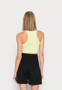 Top cropped ribbed verde claro com um design ajustado e estilo de costas nadadora, combinado com calções pretos de cintura alta.