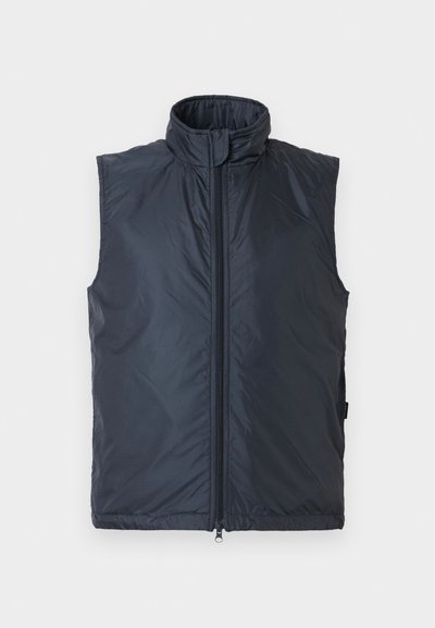 Tamsiai mėlynas pūstasis liemenė, su aukšta apykakle, užtrauktuku priekyje ir lygiu, blizgiu paviršiumi. Rankovių neturinti, skirta dėvėti sluoksniu.