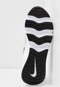 Niken lenkkarin pohja, jossa musta aaltoileva kumikuvio, kaareva valkoinen välipohja ja beige yläosa.