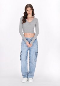 Szürke bordás, hosszúujjú crop top V-kivágással és ráncolt részletekkel, világoskék, laza szabású cargo farmernadrággal, oldalsó zsebekkel.