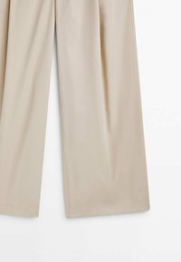 Pantalon large beige à finition lisse, détails de coutures visibles et ourlet droit sur un fond blanc.