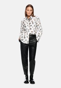 White shirt with animal prints, long sleeves, and a collar paired with black leather trousers and black boots. Simple, structured design.