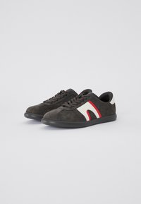 Sneakers in suede grigio scuro con un accento curvo bianco e rosso, dotate di punta arrotondata e suola in gomma nera. Design classico con lacci.