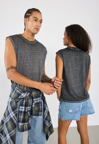 Grå ermeløse T-skjorter med heathered tekstur, kombinert med lyse denimshorts. En rutete skjorte knyttet rundt livet gir et lagdelt preg.