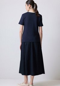 Marine T-shirt med korte ærmer og rund halsudskæring, parret med en lang, flydende nederdel. Ensartet tekstur, uden synlige mønstre eller accenter.