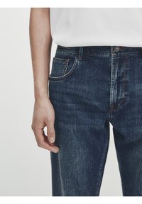 Tummansiniset farkut suoralinjaisella leikkauksella, joissa on etutasku, hillityt ompeluyksityiskohdat ja klassinen vyötärö, jossa on nappisulku.