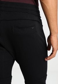 Černé joggingové kalhoty s texturovanou zadní kapsou, elastickým pasem a hladkým materiálem s přiléhavým střihem.