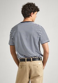 Dryžuota trumpomis rankovėmis t-marškiniai tamsiai mėlynos ir baltos spalvų, su klasikinėmis apykaklėmis. Pora su chaki spalvos kelnėmis ir juodu diržu su subtiliu tekstūru.