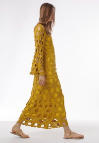 Robe maxi au crochet jaune comportant un motif floral, des manches longues et un design ajouré. Assortie à des sandales plates dorées.