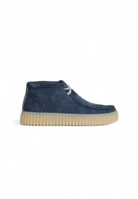 Bottines en suède bleu avec une semelle en caoutchouc. Les caractéristiques incluent un design surpiqué, un bout rond et des lacets gris. Tige texturée avec une finition lisse.