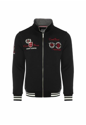 Veste de rugby noire à fermeture éclair intégrale avec logos brodés rouges et blancs sur la poitrine et la manche, poignets rayés et col montant.