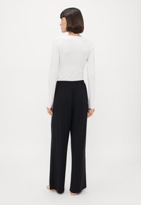 Μαύρο παντελόνι  σε φαρδιά γραμμή με ελαστική μέση, συνδυασμένο με ένα λευκό μακρυμάνικο εφαρμοστό τοπ, προβαλλόμενο από πίσω σε λευκό φόντο.