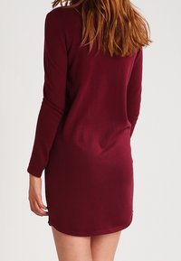 Abito a maniche lunghe color bordeaux in tessuto morbido, aderente nella parte superiore con una leggera svasatura verso l'orlo, dotato di scollatura rotonda e cuciture minime.