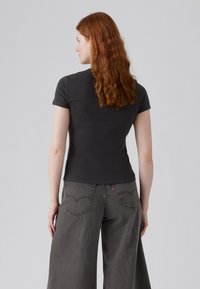 Zwarte t-shirt met korte mouwen, aansluitend design, gladde textuur. Gecombineerd met losse, grijze wijdvallende jeans met kenmerkende stiksels op de achterzak.