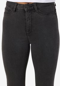 Juodi džinsai iš džinso su aukštu liemeniu, klasikiniu penkių kišenių dizainu ir subtiliu blukimu. Baigti metaliniu mygtuku ir užtrauktuko uždarymu.